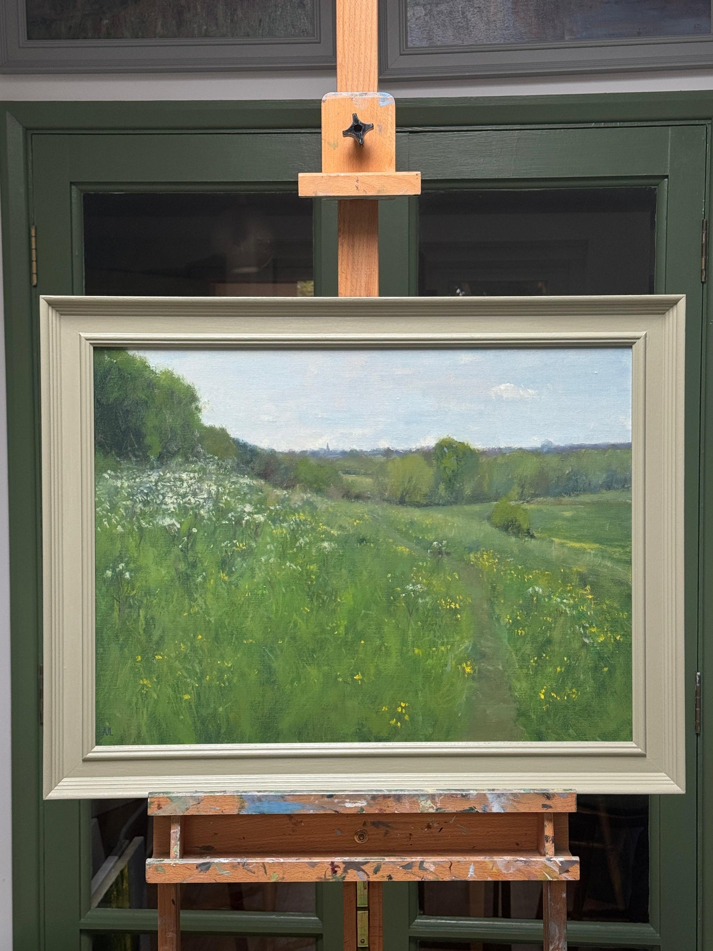The original painting in a green wooden frame presented on an easel in the artist's studio.