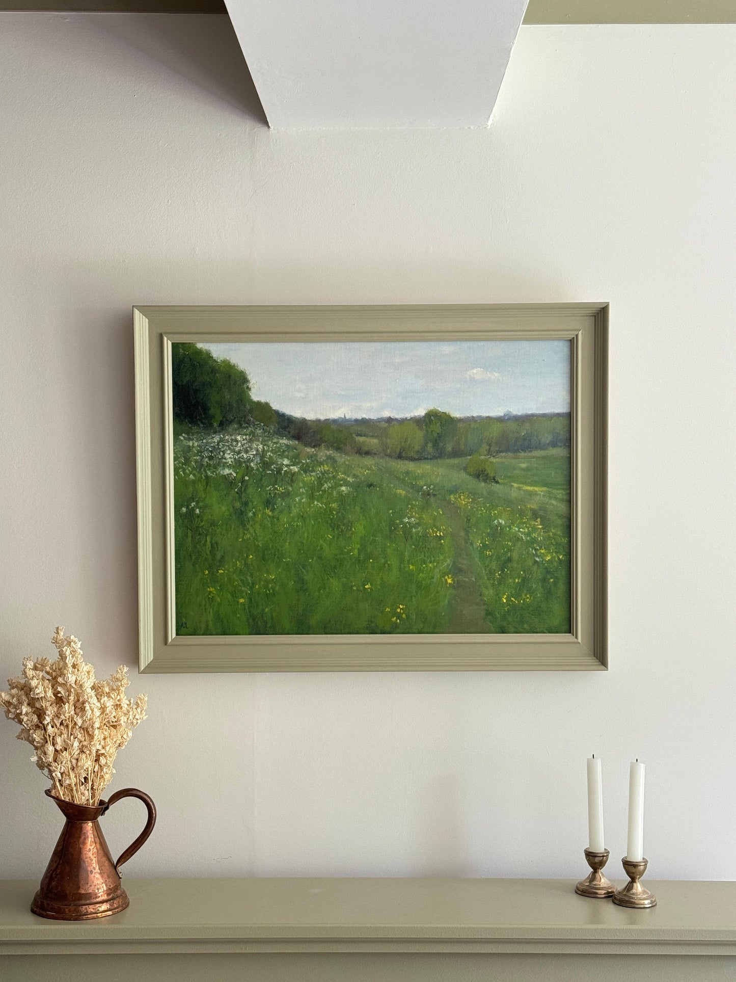 The oil painting in a green wood frame on a white wall.