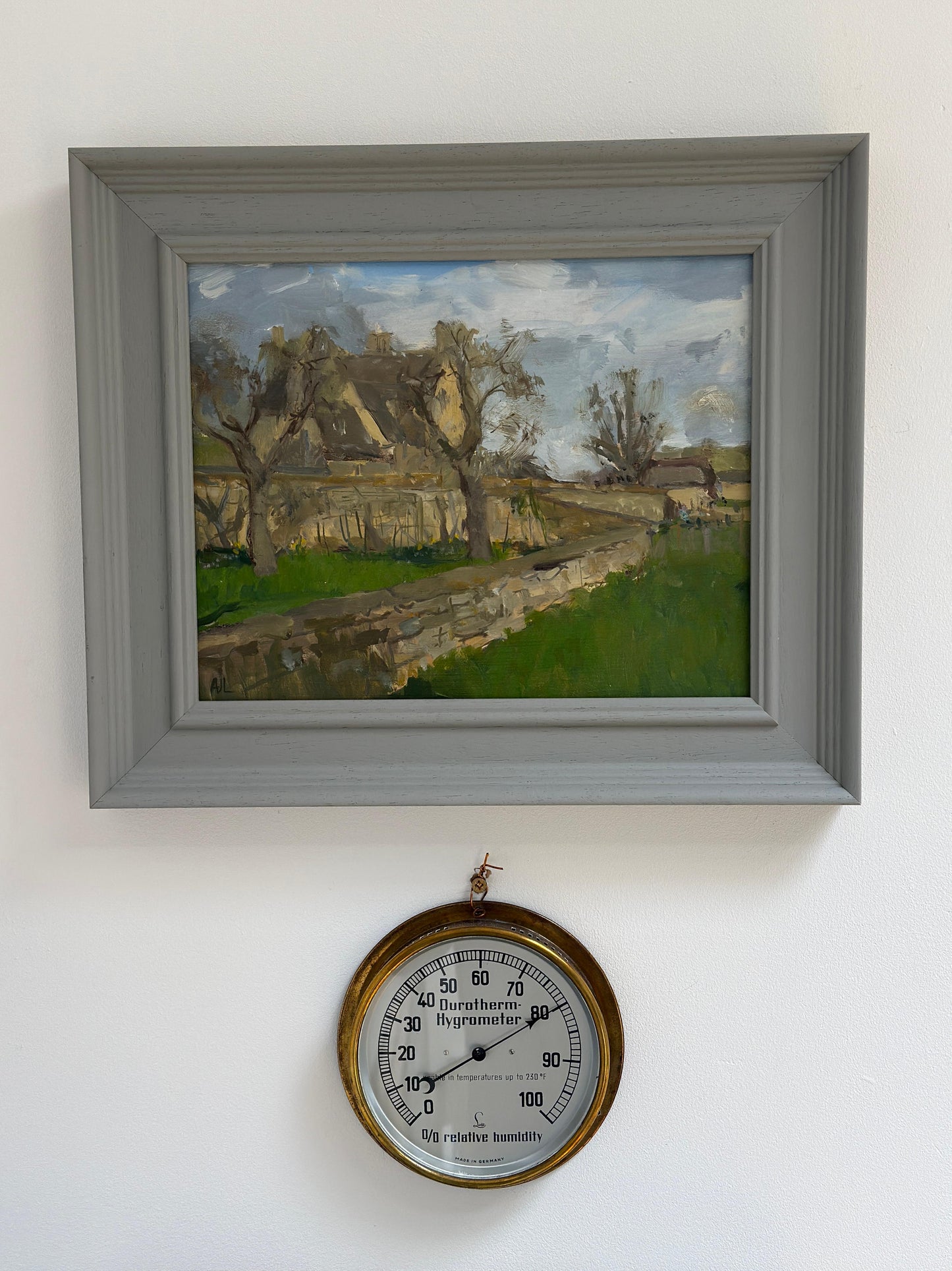 The original artwork in a grey wood frame hanging on a white wall.