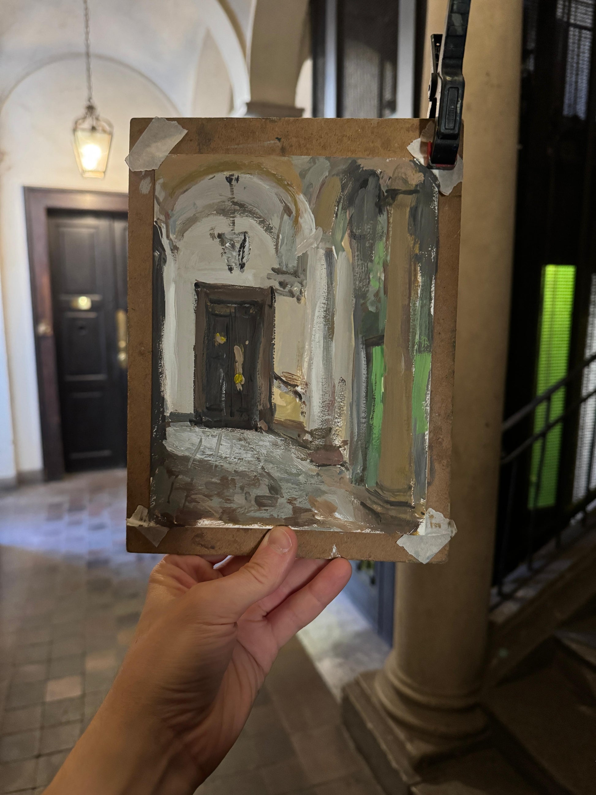 Hand holding a small painting of an architectural scene in an Italian hallway.