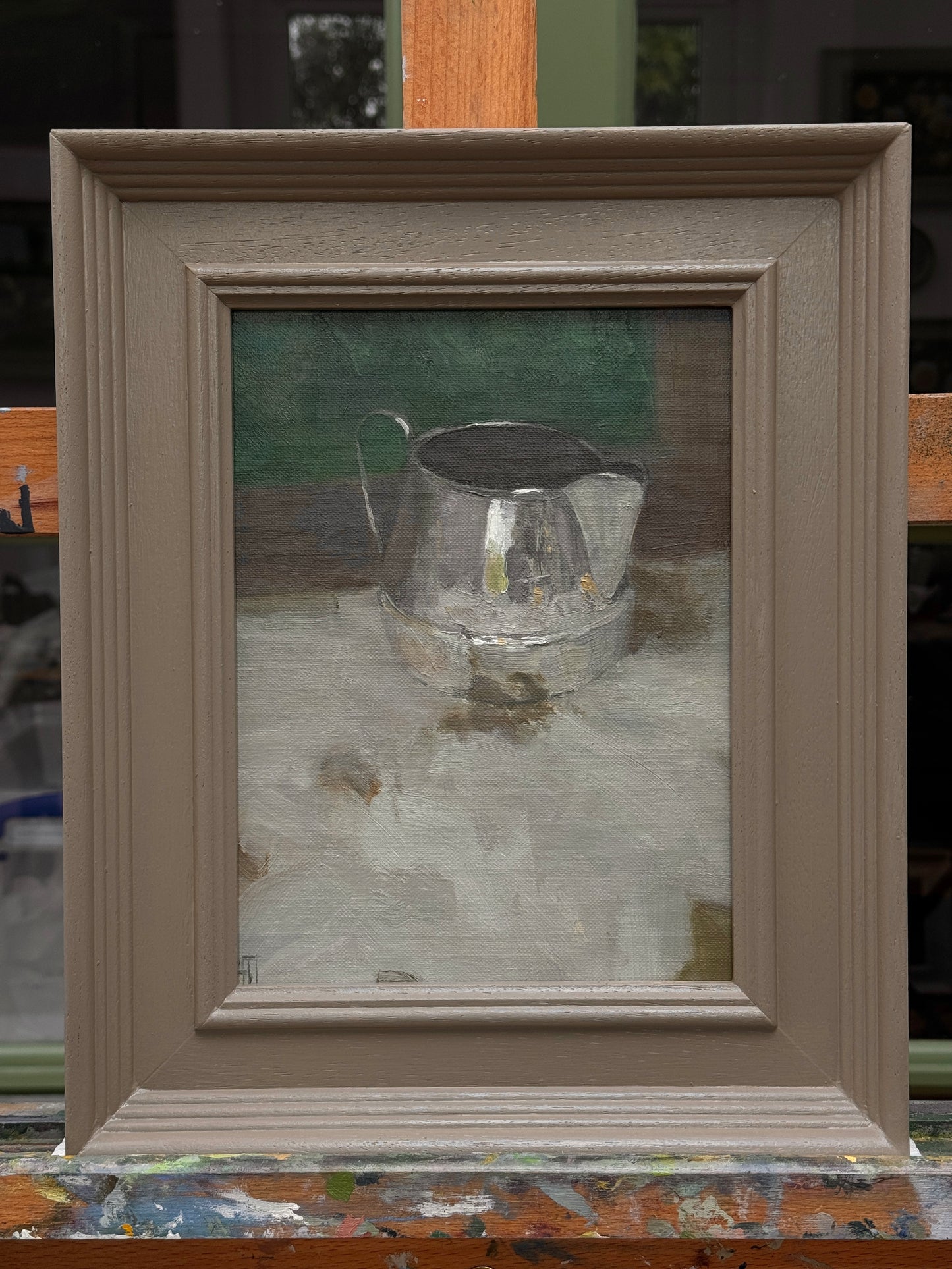 The framed still life sitting on the artist's easel.