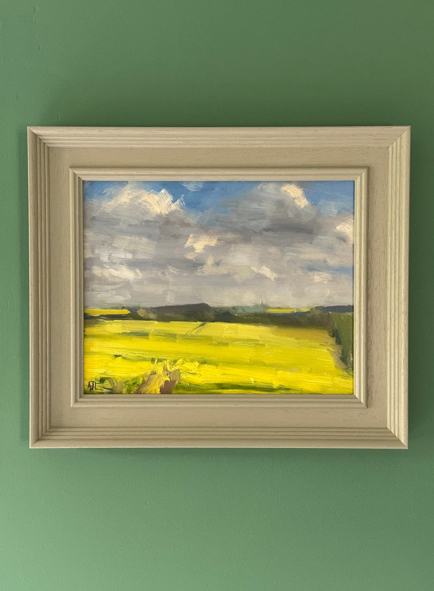 The framed oil painting hanging on a green wall.