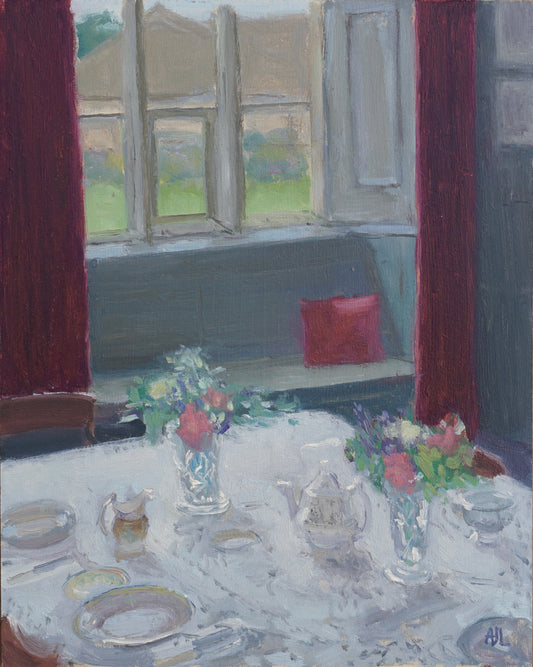 An original oil painting of the Cogges Manor Farm dining room. In the foreground is a table set with a tea service and two vases of colourful cut flowers, and in the background is a large window with deep red curtains and matching pillow on a window seat. The artist has signed AJL in blue, for "Alex James Long", at the bottom right of the artwork. 
