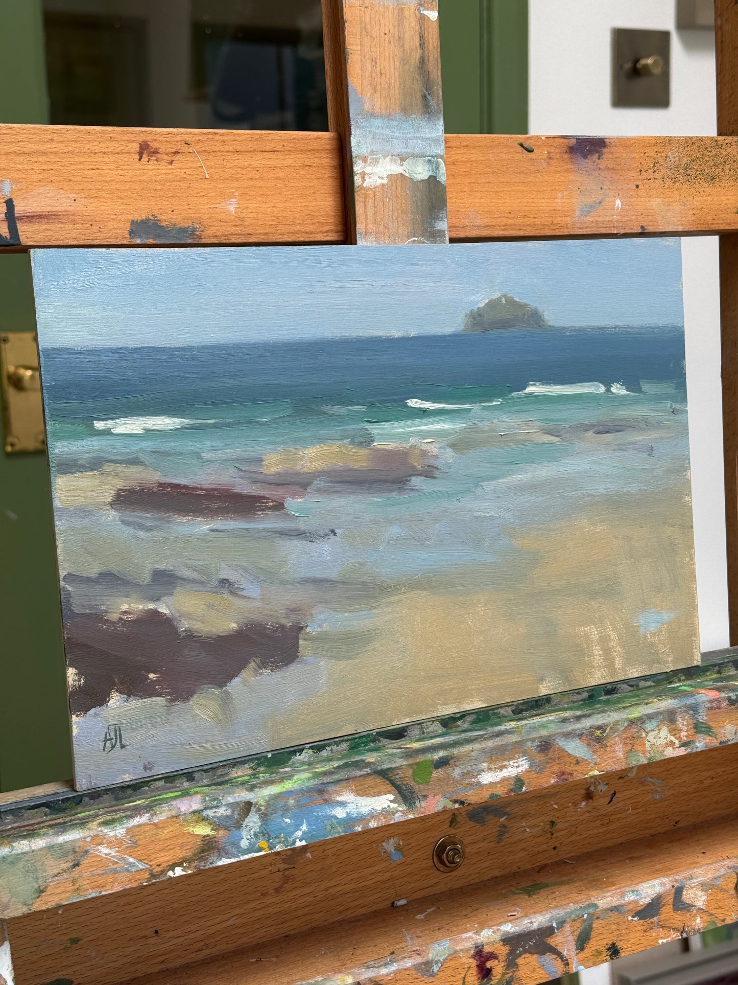A small landscape painting, featuring blue, beige, and brown brushstrokes, displayed on a wooden artist easel.