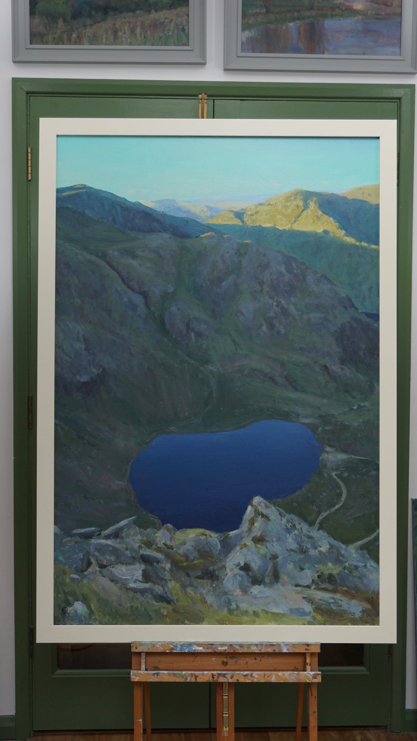 Framed painting of a mountain landscape with a blue lake on an easel.