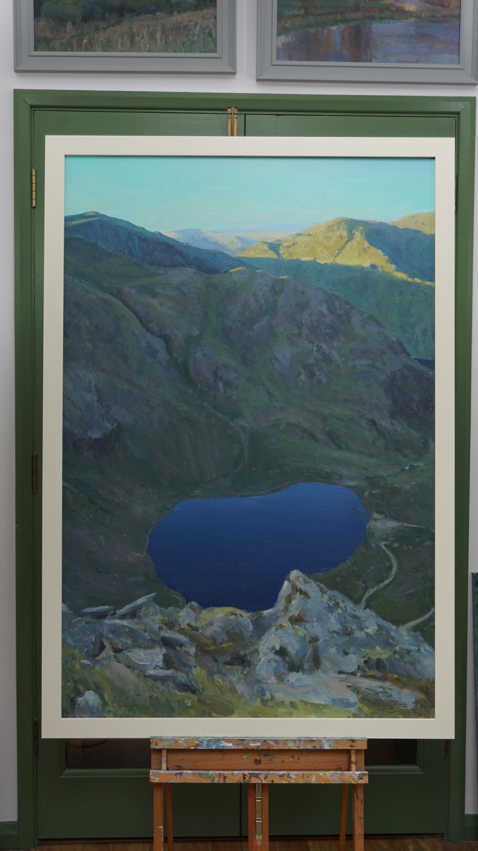 Framed painting of a mountain landscape with a blue lake on an easel.