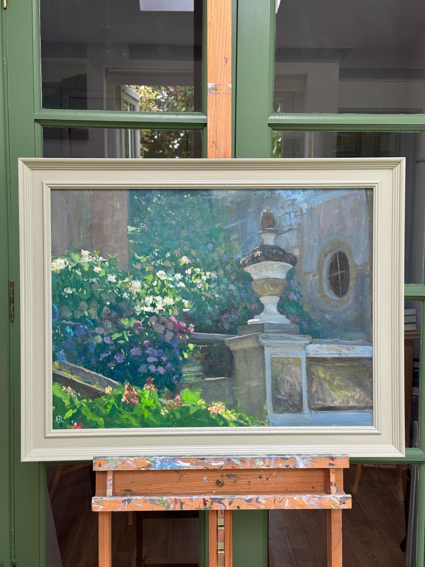 Framed painting of a garden scene on an easel against a window.