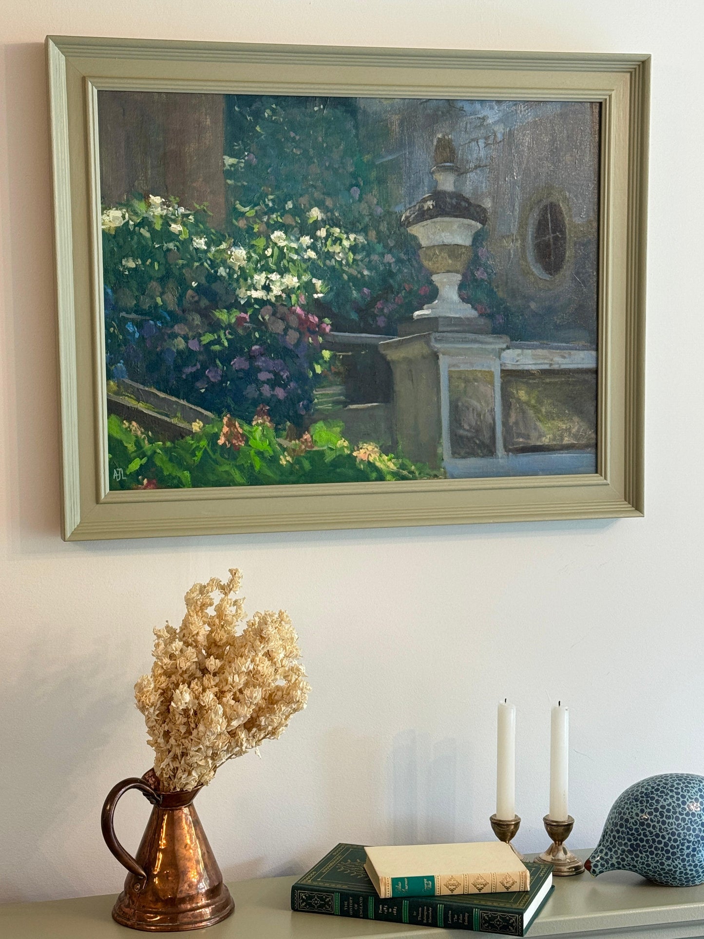 Framed painting of a garden scene on a wall above a table with decorative items.