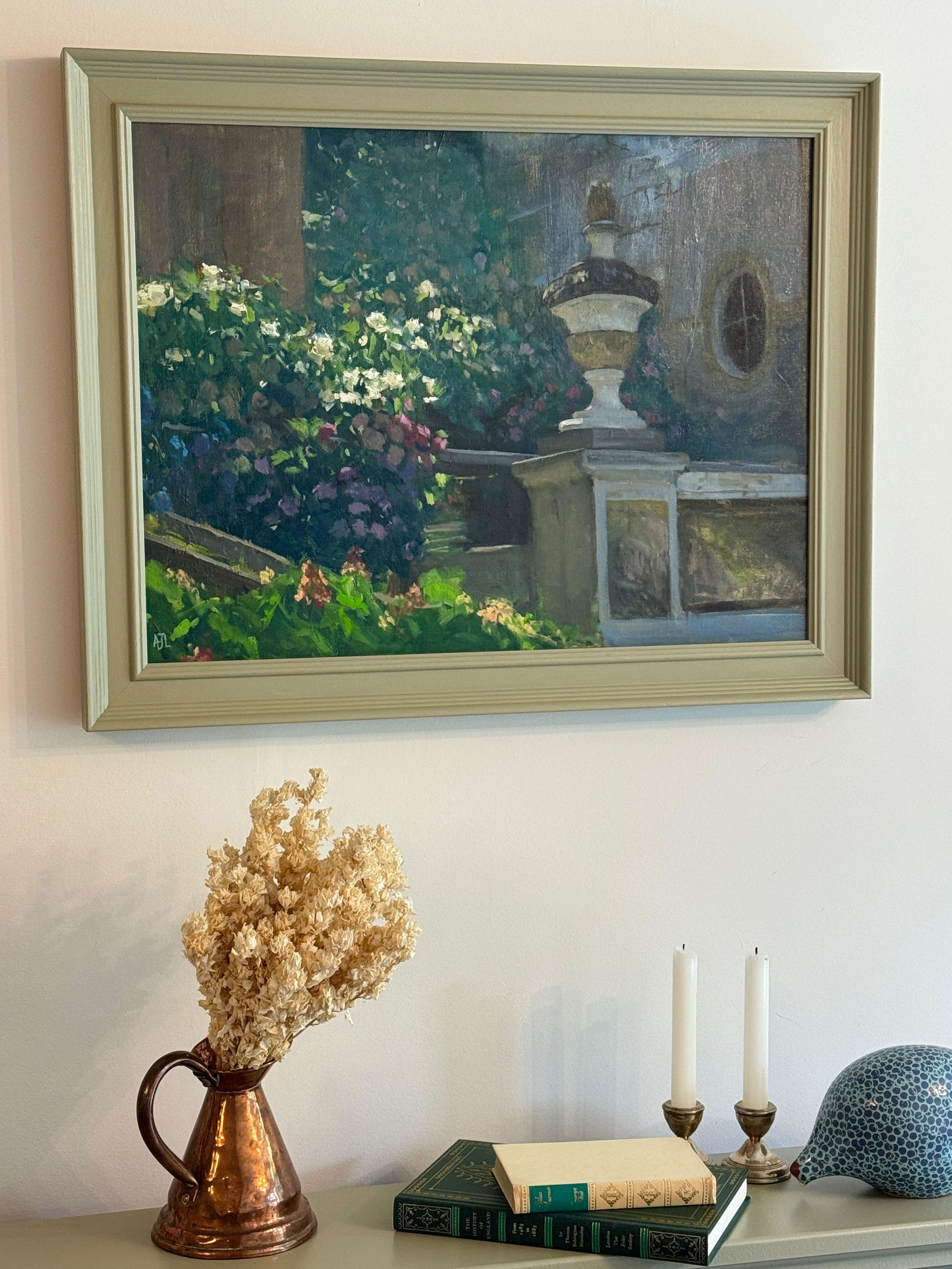 Framed painting of a garden scene on a wall above a table with decorative items.