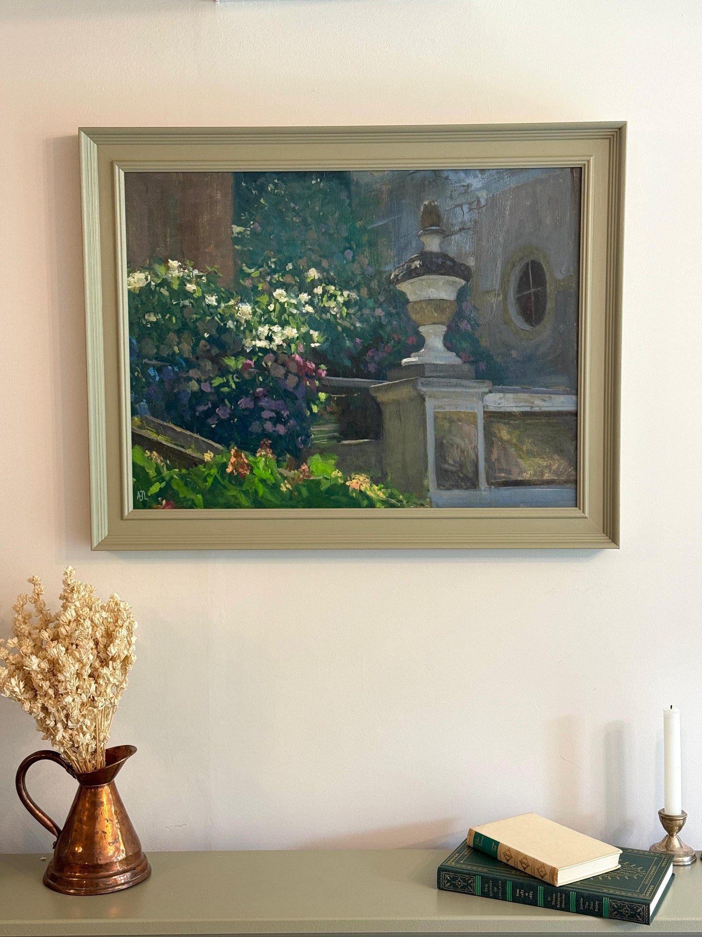 Framed painting of a garden scene on a wall above a shelf with decorative items.