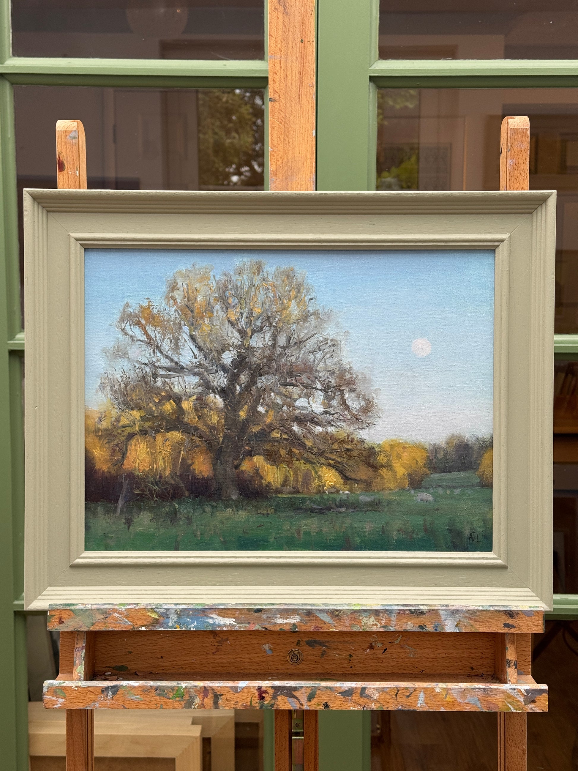 Framed painting of a landscape with trees and a moonlit sky, displayed on a wooden surface.