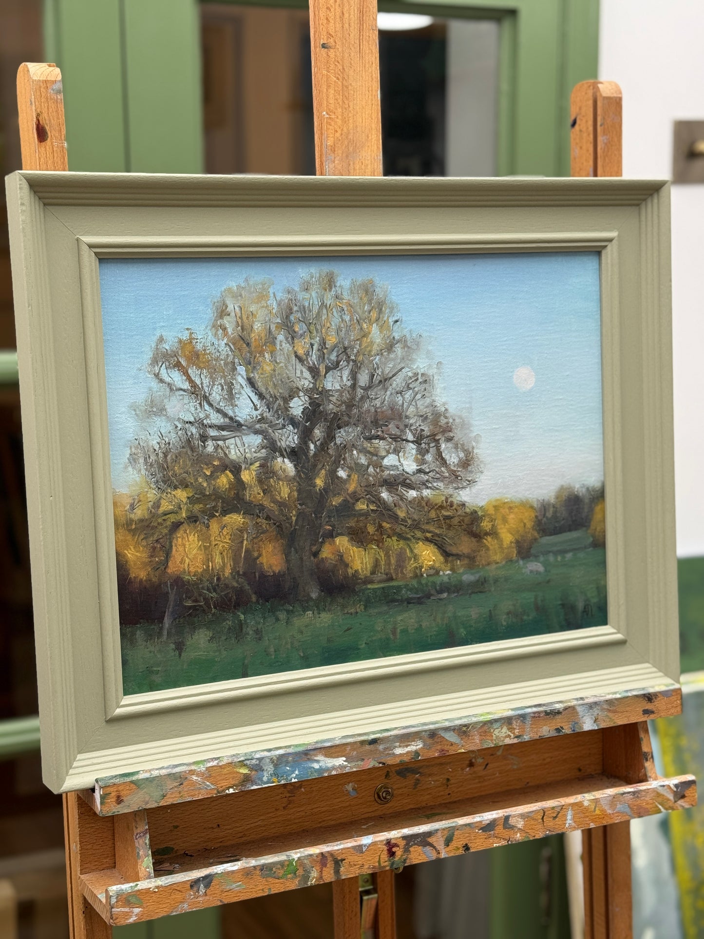 Painting of a tree in a field on an easel with a green background