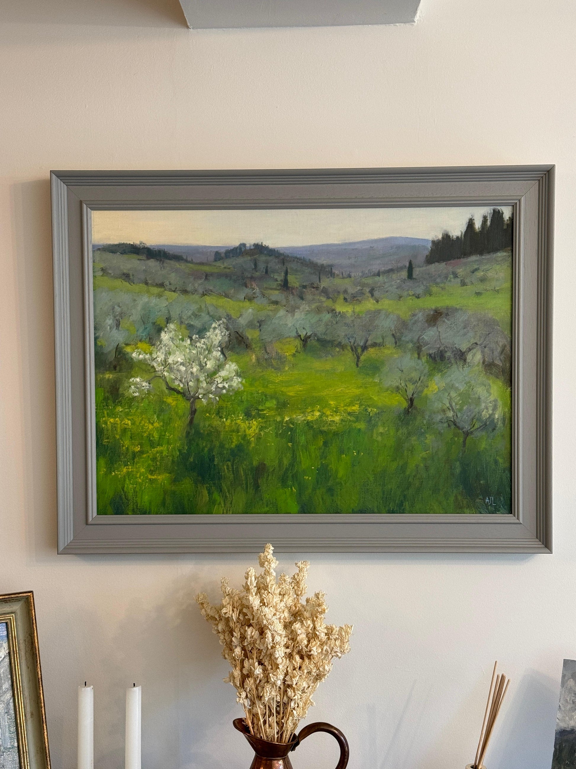 A photograph of the original oil painting, framed and hanging on a white wall. 