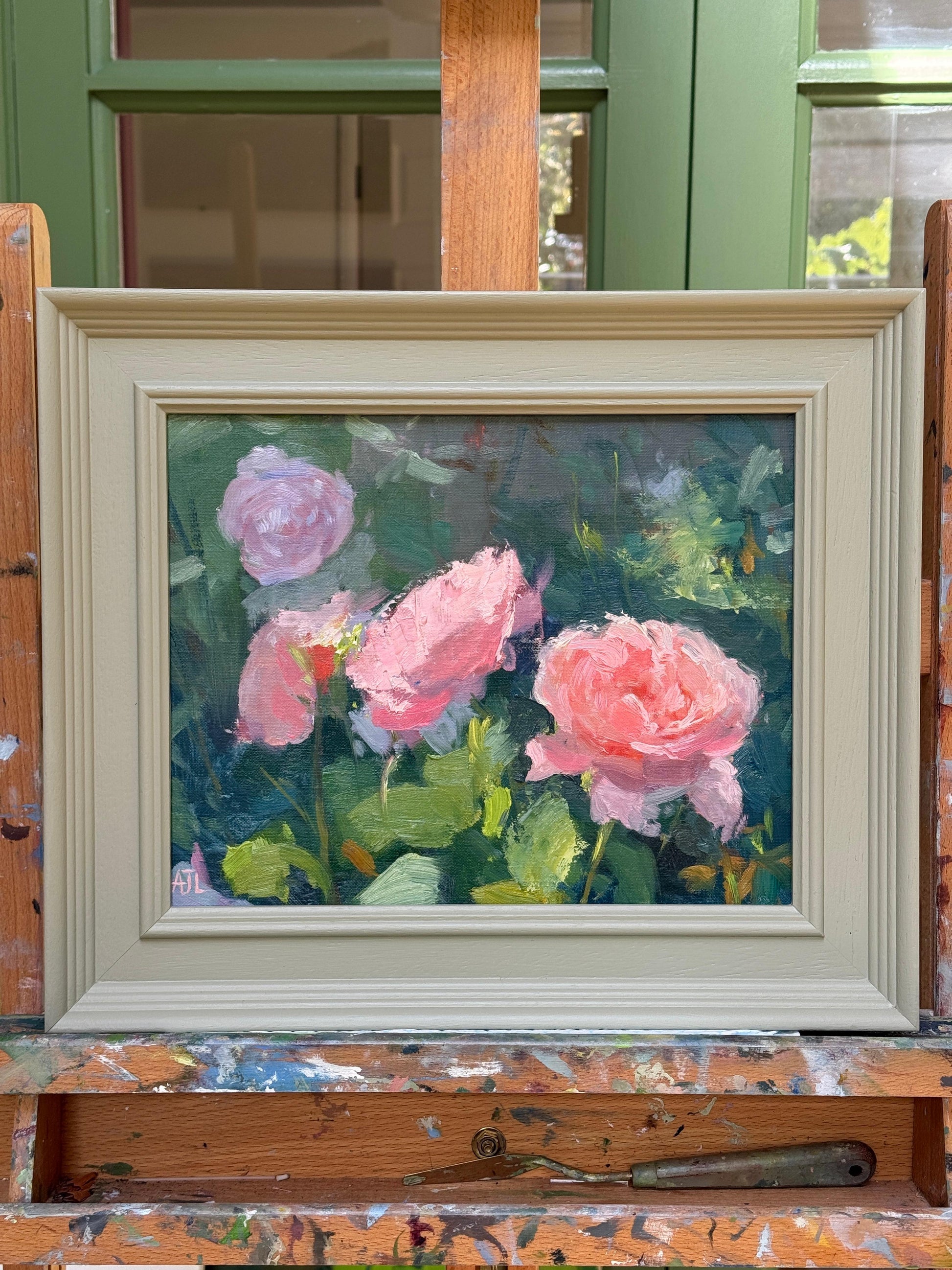 Framed painting of pink flowers on a wooden easel.