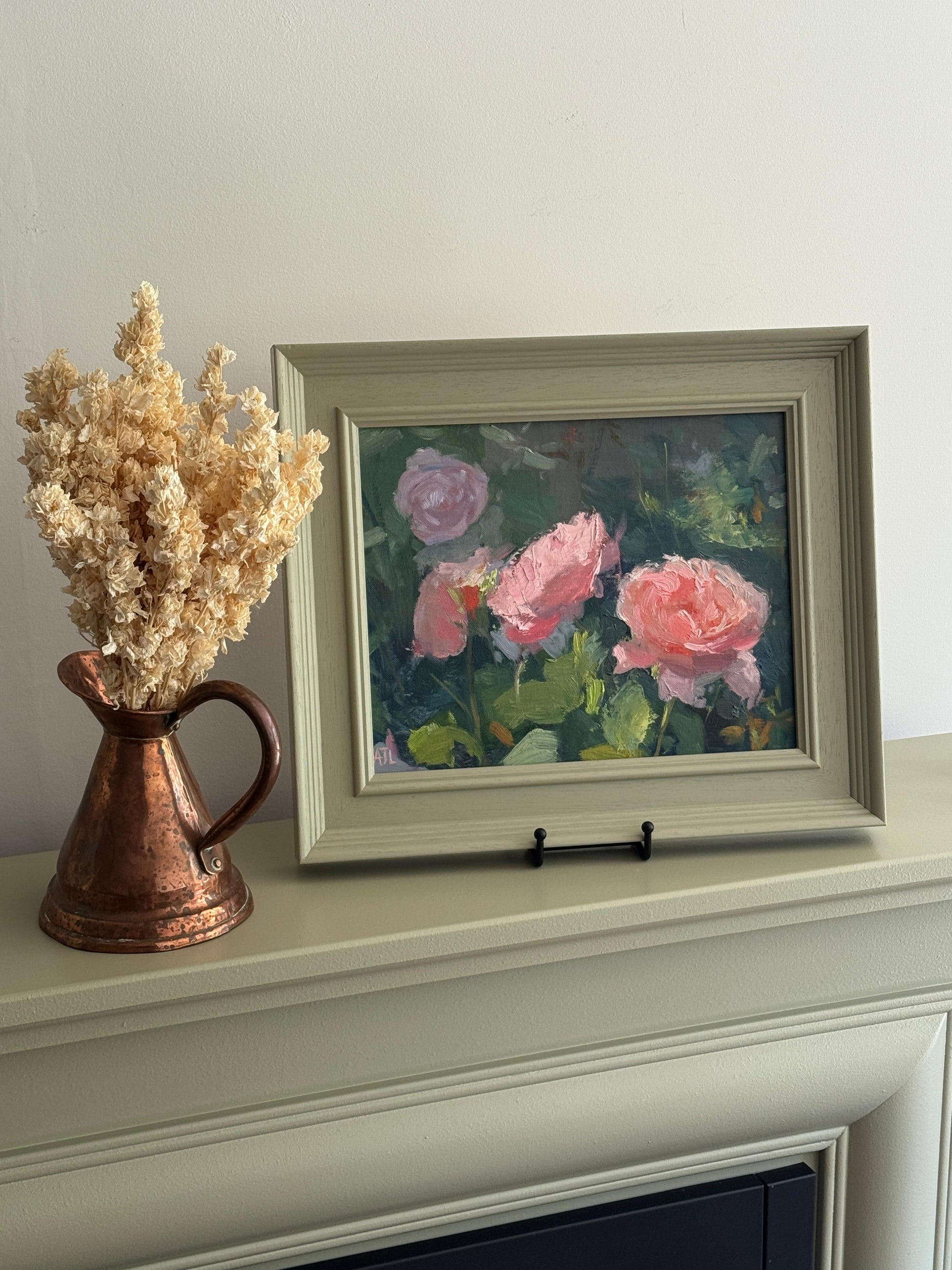 Framed painting of pink roses on a mantelpiece with a copper pitcher and dried flowers.