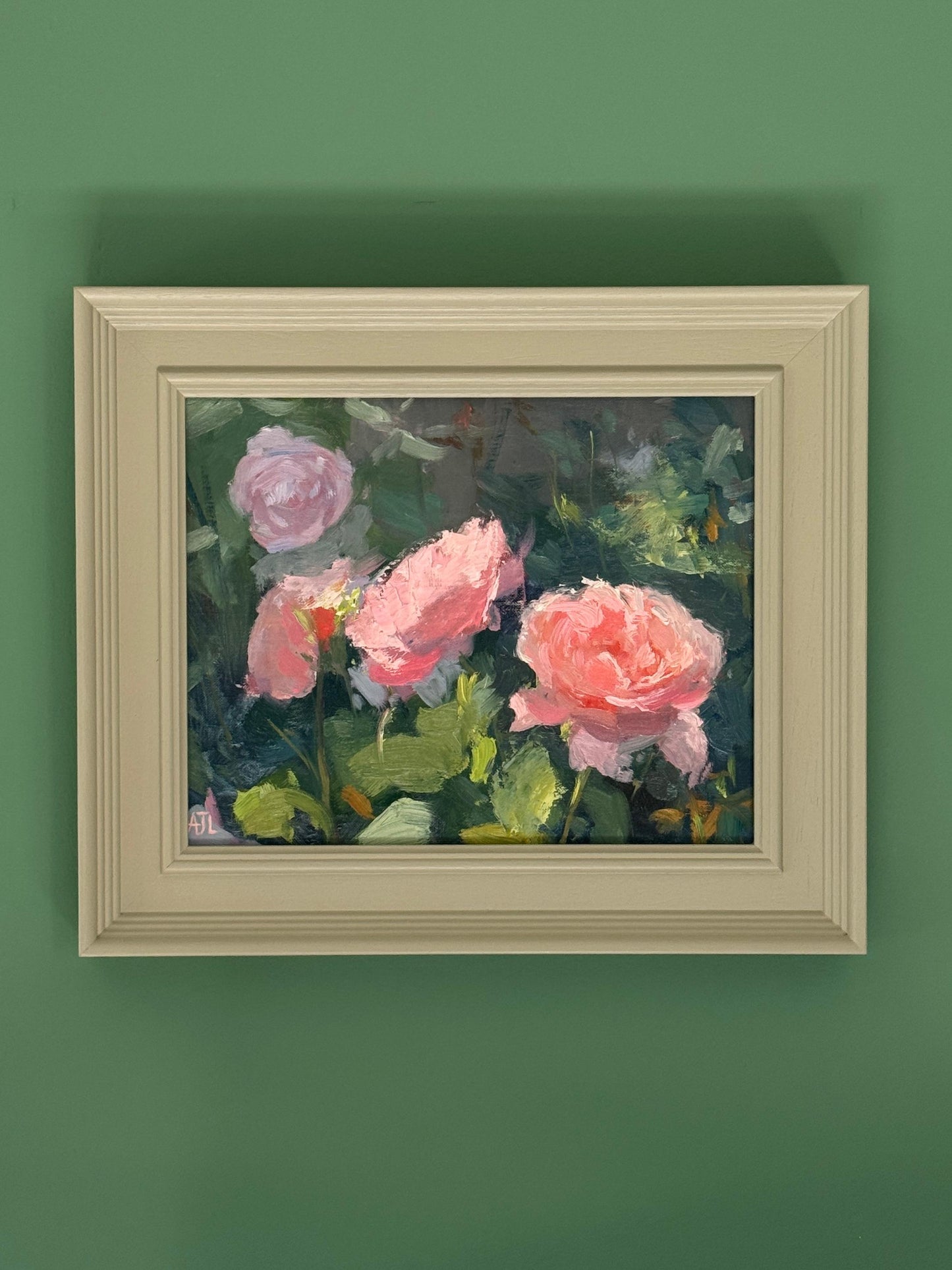 Framed painting of pink roses on a green wall.