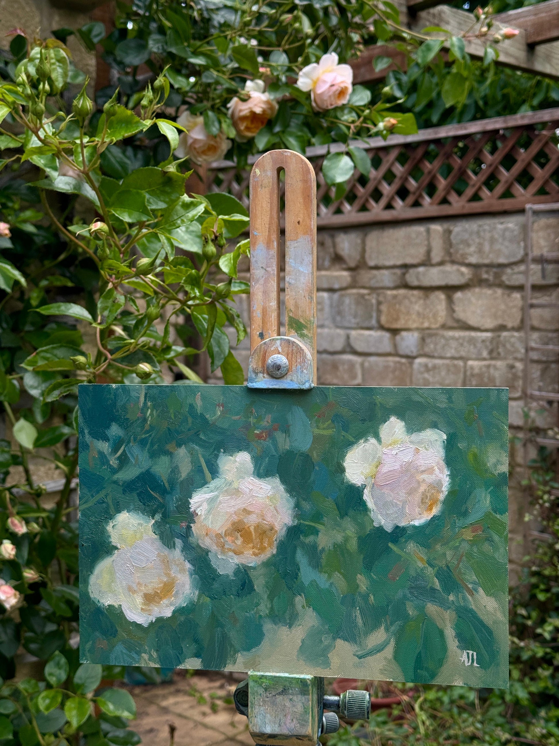 The original artwork on an easel outside, near the three roses depicted in the painting.