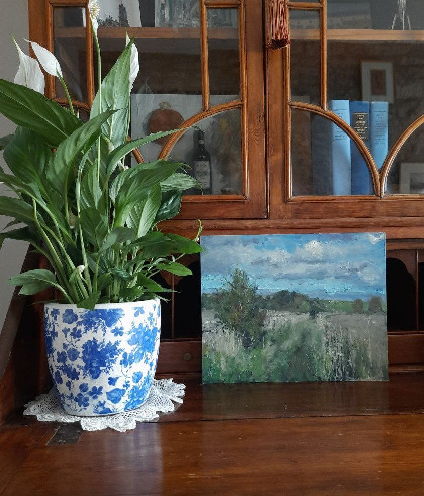 The painting upon a wood secretary bookcase and next to a potted plant.