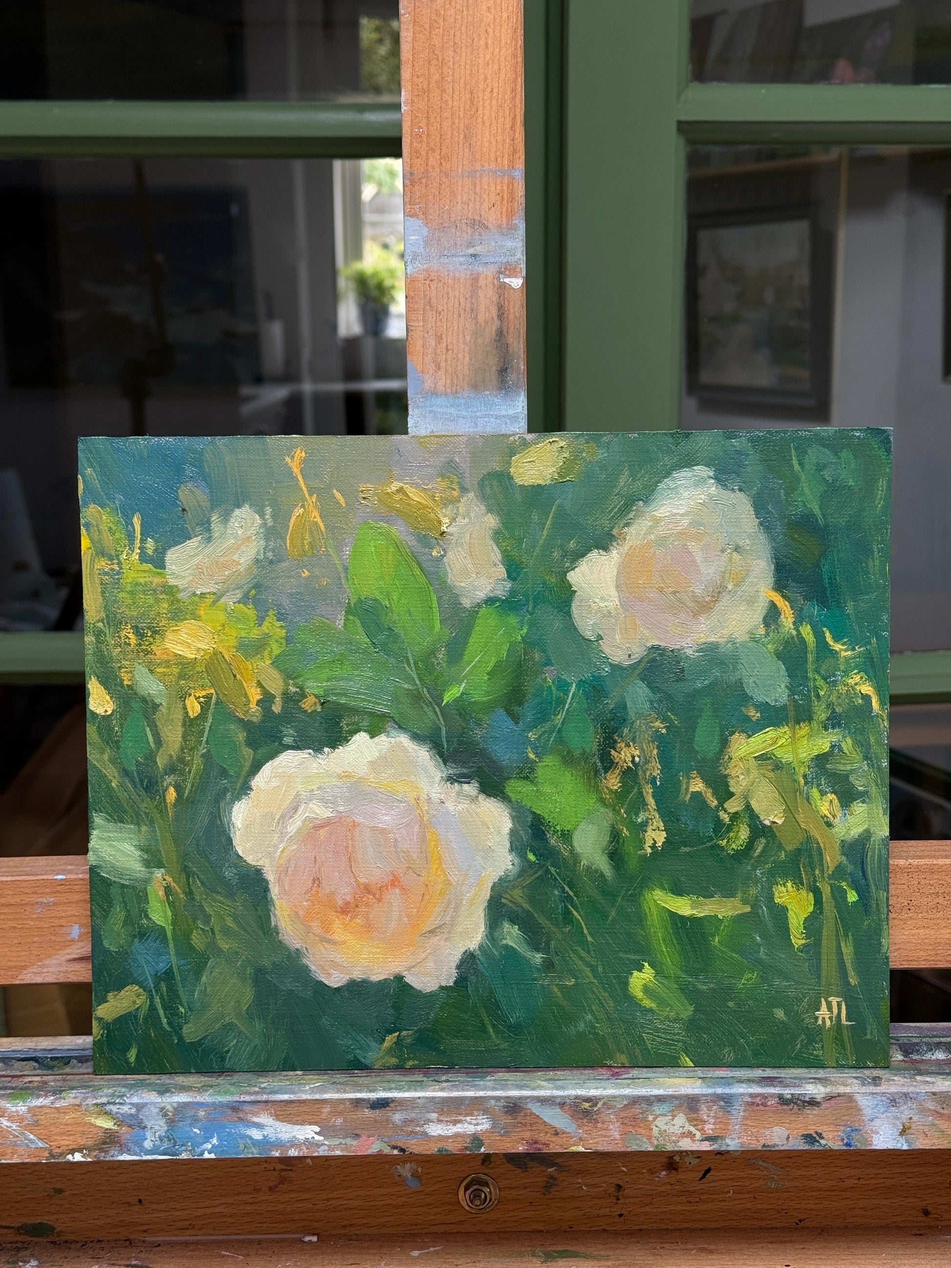 Oil painting of flowers on an easel with a blurred indoor background.