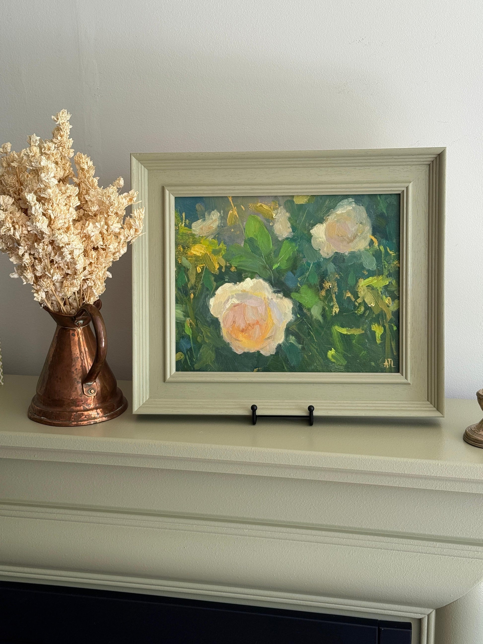 Framed painting of flowers on a white surface with a decorative copper vase.