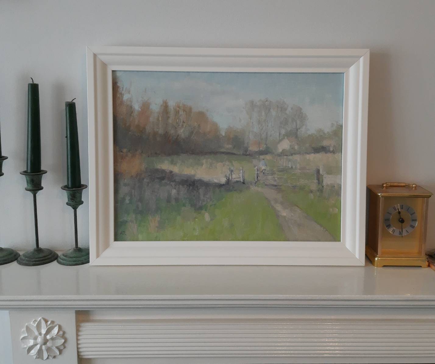 The artwork in a white wooden frame on a mantle.